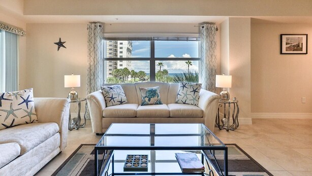 A living room with a beige sofa, a glass coffee table, and a view of the ocean through large windows.