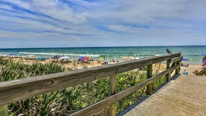 A wooden boardwalk leading to a beach with umbrellas and people.