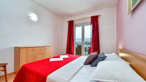 Ein Hotelzimmer mit einem Bett, einem hölzernen Schminktisch und Blick auf ein Gewässer durch ein Fenster mit roten Vorhängen.