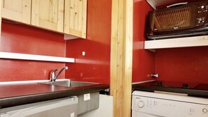 Een kleine keuken met houten kastjes, een spoelbak, een vaatwasser en een fornuis.
