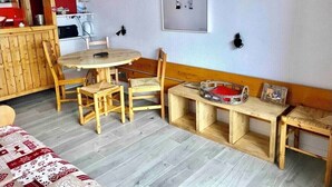 Een gezellige kamer met een houten eettafel, stoelen, een klein bankje en een boekenkast.
