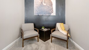 Ein Zimmer mit zwei Sesseln, einem kleinen Beistelltisch und einem Wandbild eines Bisons.