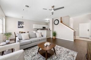 Un salon moderne avec un canapé gris, une table basse en bois et un coin repas comprenant une table et des chaises blanches.