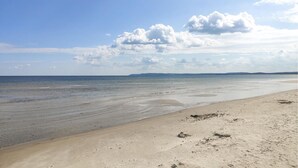 A wide sandy beach with gentle waves, a clear sky, and distant landforms.