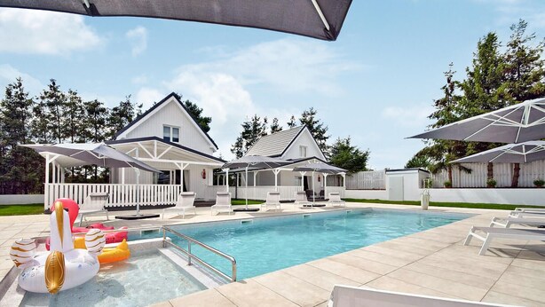 A swimming pool with lounge chairs and umbrellas, surrounded by a white house with a covered patio.