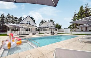 A swimming pool with lounge chairs and umbrellas, surrounded by a white house with a covered patio.