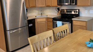 A modern kitchen with wooden cabinets, stainless steel appliances, and a wooden dining table. - Cute Condo in the heart of OCNJ  (Ocean City)