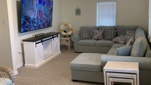 A living room with a grey sofa, a television, a ceiling fan, and a small side table. - Cute Condo in the heart of OCNJ  (Ocean City)