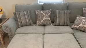 A grey sectional sofa with patterned cushions, a small wooden side table, and a wall decoration. - Cute Condo in the heart of OCNJ  (Ocean City)