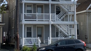 A two-story building with a balcony on the second floor, a front porch, and a staircase leading to the upper floor. - Cute Condo in the heart of OCNJ  (Ocean City)