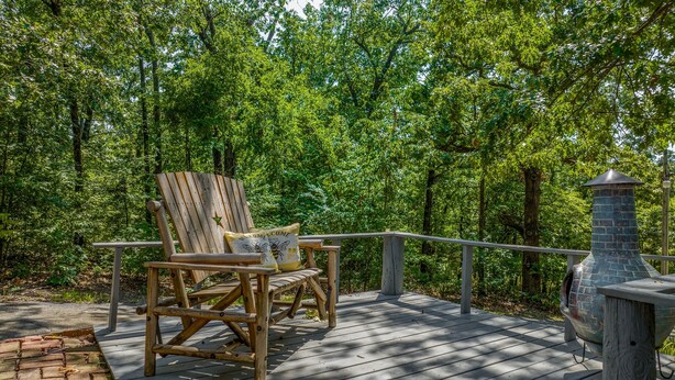 A wooden deck with a wooden chair and a stone fireplace. - Lake Views & Fall Colors | Cozy Cottage + Kayaks (Jay)