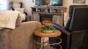 Ett mysigt vardagsrum med en soffa, ett litet runt bord med en växt, en tv och en öppen spis.