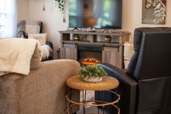 A cozy living room with a sofa, a small round table with a plant, a television, and a fireplace. - Lake Views & Fall Colors | Cozy Cottage + Kayaks (Jay)