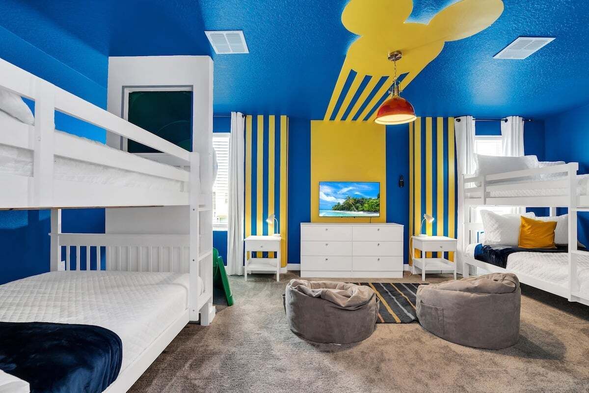Una habitación con literas, un aparador blanco, un escritorio y un sillón de plumas.