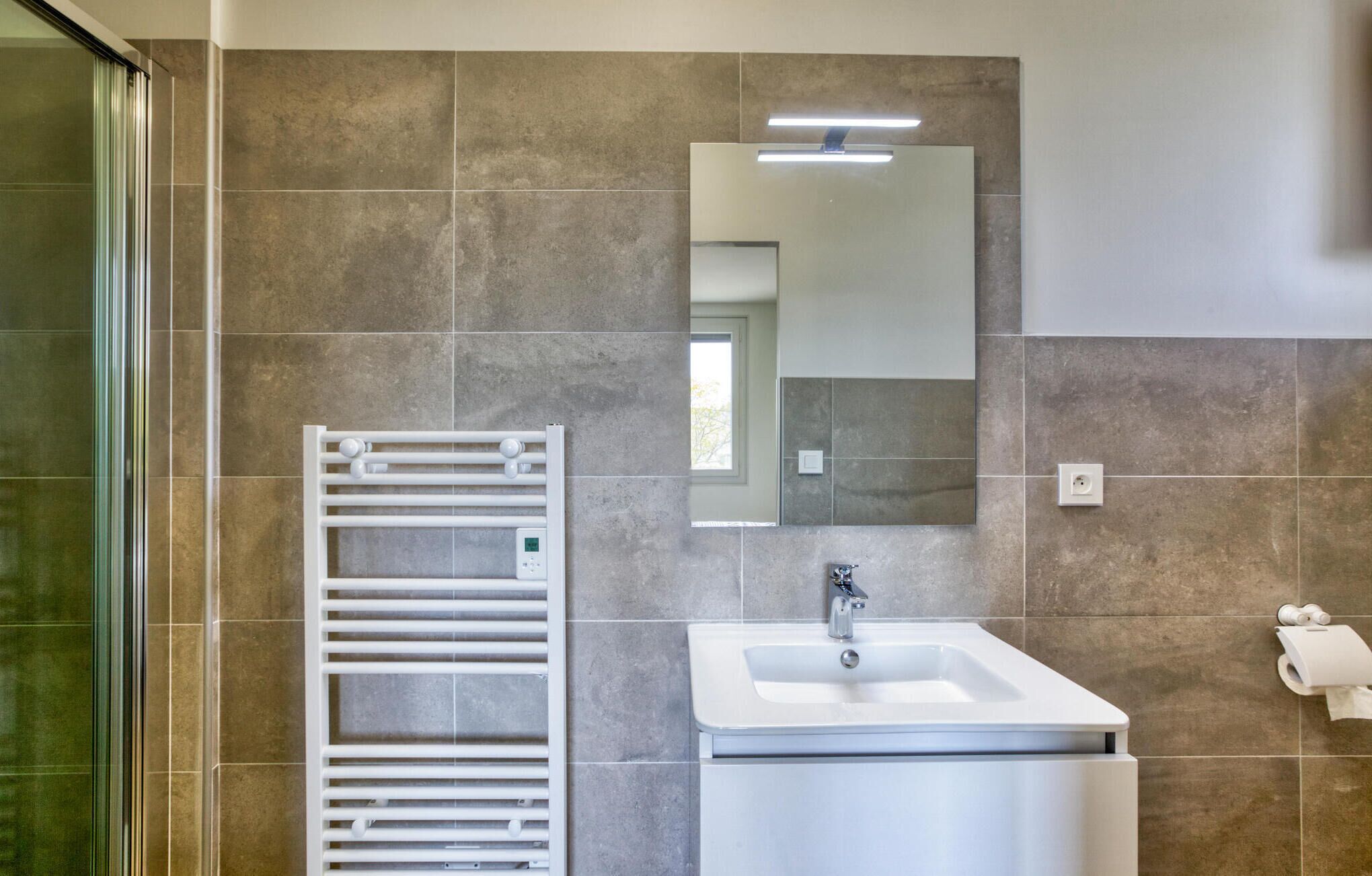 A modern bathroom with a built-in shower, a white sink, and a towel rack.