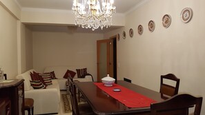 A dining room with a long table, chairs, a chandelier, and a sofa with cushions.
