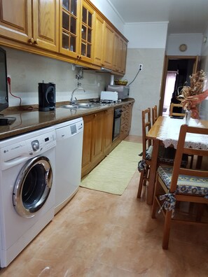 A kitchen with wooden cabinets, a washing machine, a microwave, and a dining area with a table and chairs.