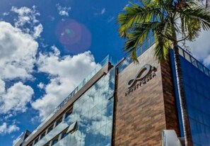 Um hotel moderno com fachada de vidro que reflete o céu e as nuvens.