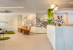 Uma área de recepção moderna com balcão de mármore, poltronas de espera e um mural na parede.