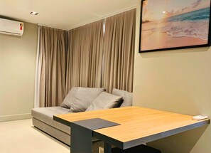 Quarto de hotel moderno com sofá, mesa de madeira e pintura de uma paisagem praiana.