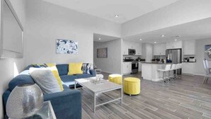 A modern living room with a sofa, coffee table, and ottomans. There is a kitchen area with a bar and seating. - Fun gameroom,big yard,pool+spa,fire pit (Desert Hot Springs)