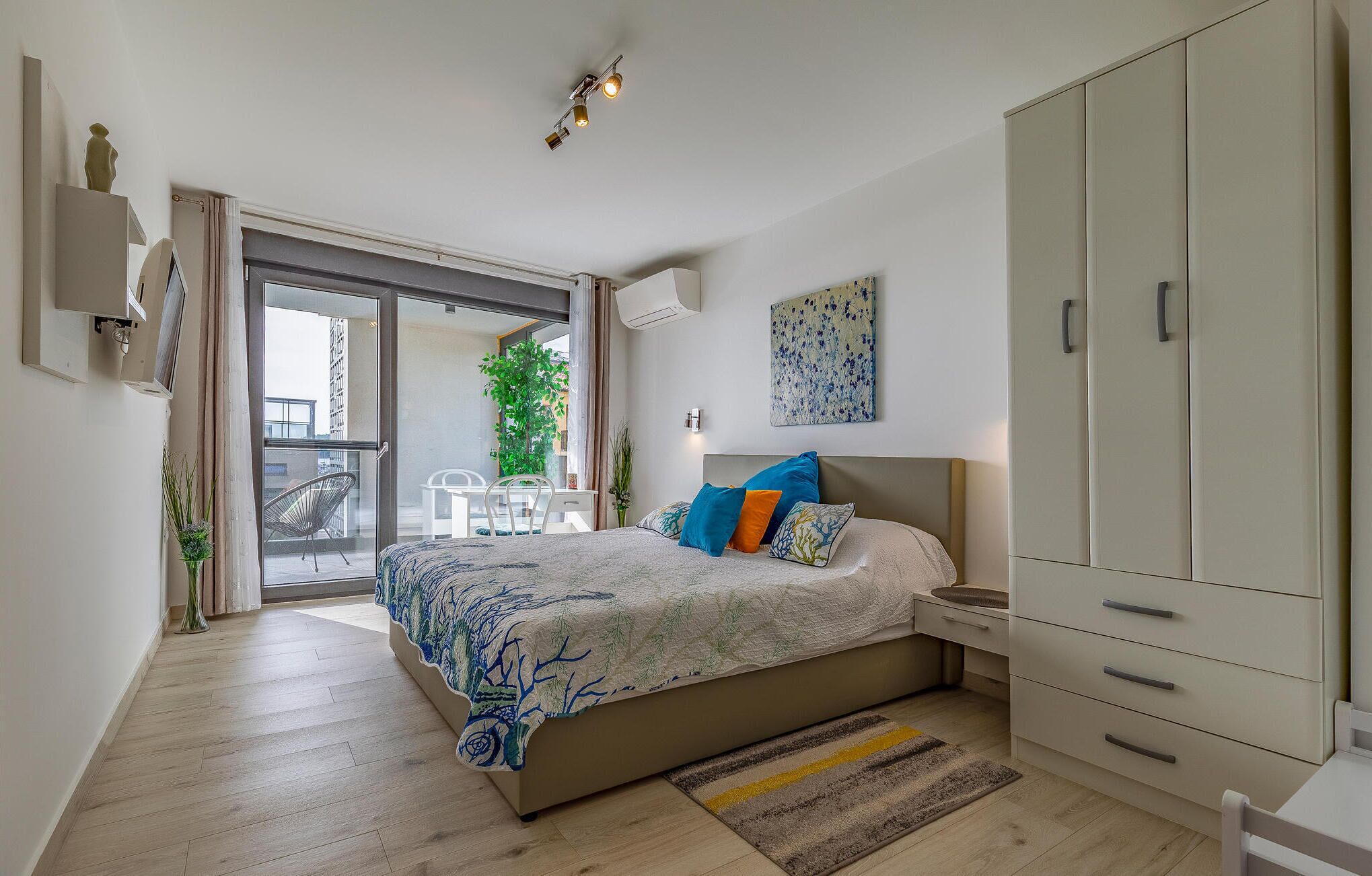 Una camera da letto con un letto, un armadio, un balcone con tavolo e sedie, e una pianta in vaso.