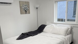 A bedroom with a bed, a painting, a floor lamp, and a window.