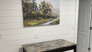 A dining area with a table and two chairs, a painting on the wall, and a door in the background.