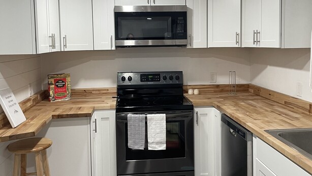 A kitchen with white cabinets, a black microwave, a stove, and a dishwasher.