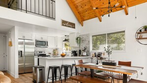 Una cocina moderna con armarios blancos, electrodomésticos de acero inoxidable y una mesa de comedor de madera con taburetes de bar.
