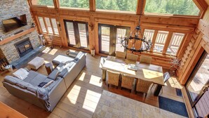 A spacious cabin with a stone fireplace, a large dining table with wicker chairs, and a cozy seating area with a sofa and ottoman. - Chalet Belle Cordélia with Spa and AC (Nominingue)