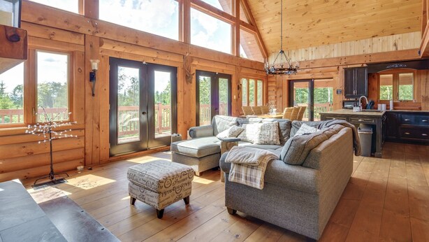 A spacious cabin with large windows, a cozy living area with a sofa and ottoman, a dining area, and a kitchen with wooden cabinets. - Chalet Belle Cordélia with Spa and AC (Nominingue)