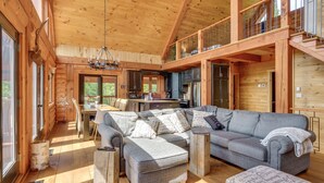 A spacious log cabin interior with a large gray sectional sofa, a dining area, and a kitchen. - Chalet Belle Cordélia with Spa and AC (Nominingue)
