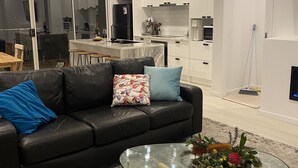 A modern living room with a black leather sofa, a glass coffee table with a floral centerpiece, and a kitchen in the background. - Brand new upside down townhouse with ocean views (Ventnor)