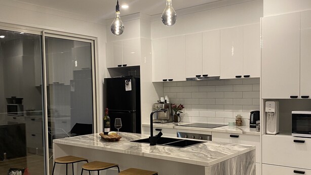 A modern kitchen with a marble island, bar stools, and pendant lighting. - Brand new upside down townhouse with ocean views (Ventnor)