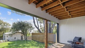 A spacious deck with a wooden floor and a glass wall offering a view of a backyard with a lawn and trees. - Brand new upside down townhouse with ocean views (Ventnor)