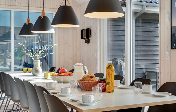 Enjoy a meal in this stylish dining area with a long table set for a meal, featuring a variety of fresh fruits, bread, and a bottle of juice.