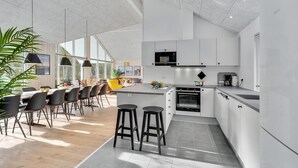 Une cuisine moderne avec des meubles blancs, un four encastré et un grand îlot central doté de tabourets.