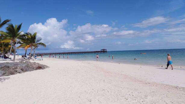 A beach with white sand, palm trees, and a pier extending into the water. - 2 Bedroom Penthouse - with Rooftop Picuzzi.3 min to the beach!! (Punta Cana)