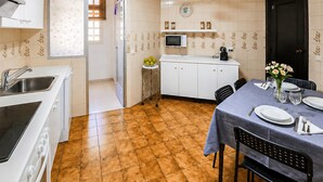 Een praktische keuken met een magnetron, spoelbak en fornuis, een eethoek met een tafel voor twee personen, en een deur naar een badkamer.
