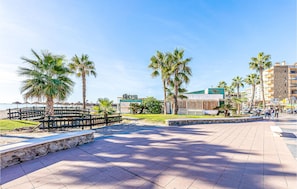 Una passeggiata lastricata con palme, una spiaggia sullo sfondo e un edificio con un cartello.