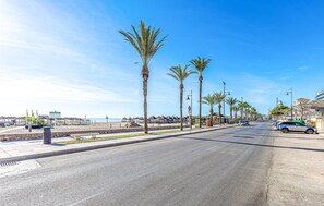 Una strada costiera fiancheggiata da palme, con una spiaggia sullo sfondo e un cielo azzurro terso.