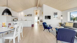 Eine moderne Küche mit weißen Schränken, ein Essbereich mit weißen Stühlen, ein blauer Sessel und ein graues Sofa.