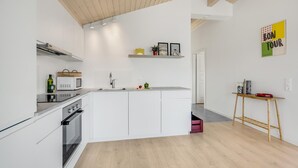 Eine moderne Küche mit weißen Schränken, einem eingebauten Ofen, einer Mikrowelle und einem Spülbecken. Die Decke ist aus Holz und es steht ein kleiner Holztisch mit einer roten Schüssel da.