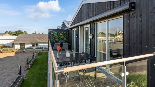 Eine moderne Außenterrasse mit Glastrennwand, einem Holztisch und einem Grill.