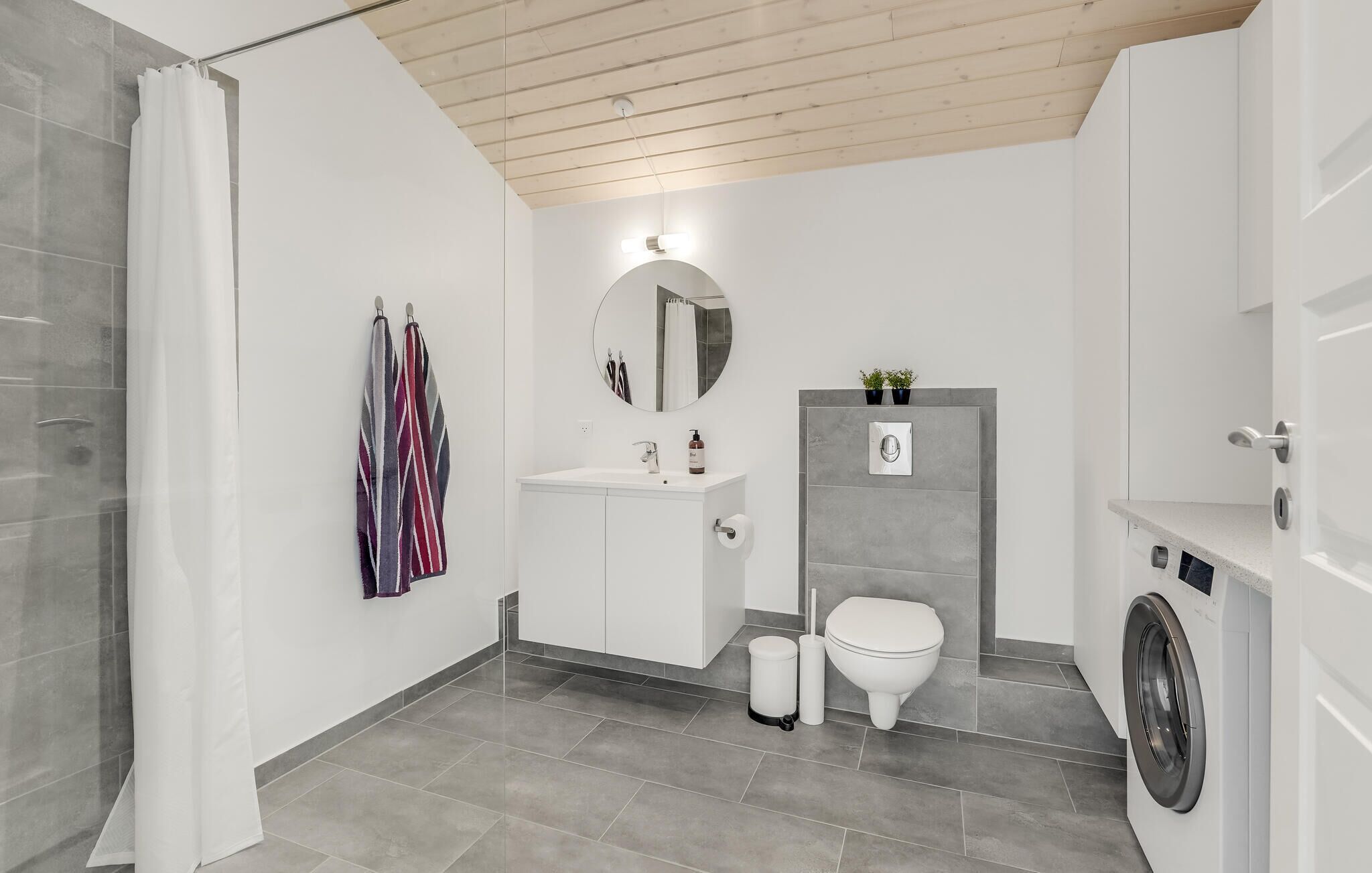Een moderne badkamer met douche, toilet, wastafel en wasmachine.