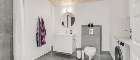 Een moderne badkamer met douche, toilet, wastafel en wasmachine.
