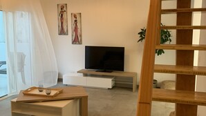 Ein modernes Wohnzimmer mit einer Holztreppe, einem Flachbildfernseher, einem Glastisch und einem großen Fenster mit durchsichtigen Vorhängen.