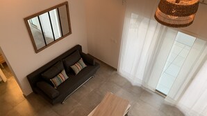 Ein modernes Wohnzimmer mit einem dunkelgrauen Sofa, einem Holztisch und einem großen Fenster mit leichtem Vorhang.
