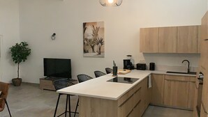 Ett modernt kök med träskåp, en köksö med barstolar, ett matbord, en tv och en hängande lampa.